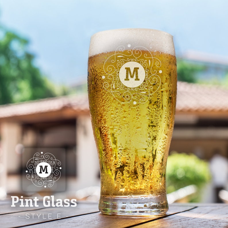 Op de afbeelding: Een bevroren pintglas gevuld met lichtgeel bier. Het glas heeft een decoratief ontwerp met de letter "M" in het midden.