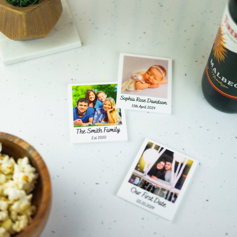 May include: Three white photo magnets with black text and images. The first magnet shows a family of four, the second shows a baby girl, and the third shows a couple. The text on the magnets reads "The Smith Family Est 2010", "Sophia Rose Davidson 11th April 2024", and "Our First Date 01.10.2014".