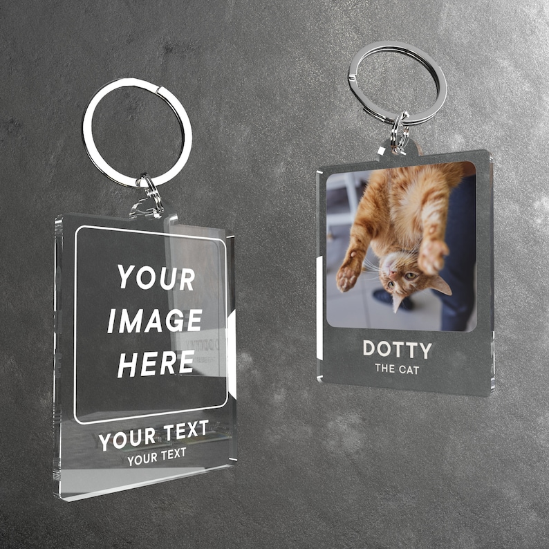 Puede incluir: Dos marcos de fotos de llavero de acr&iacute;lico transparente con llaveros plateados. El marco de la izquierda tiene el texto "YOUR IMAGE HERE" y "YOUR TEXT YOUR TEXT". El marco de la derecha tiene una foto de un gato boca abajo con el texto "DOTTY THE CAT".
