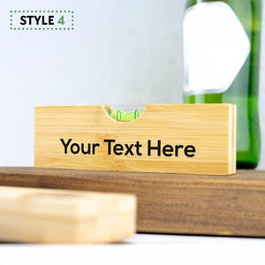 K&ouml;nnte beinhalten: Ein Holz-Wasserwaage mit einer gr&uuml;nen Libelle und dem Text "Your Text Here" auf der Vorderseite graviert. Die Wasserwaage ist aus Bambus und hat eine nat&uuml;rliche Holzoptik.