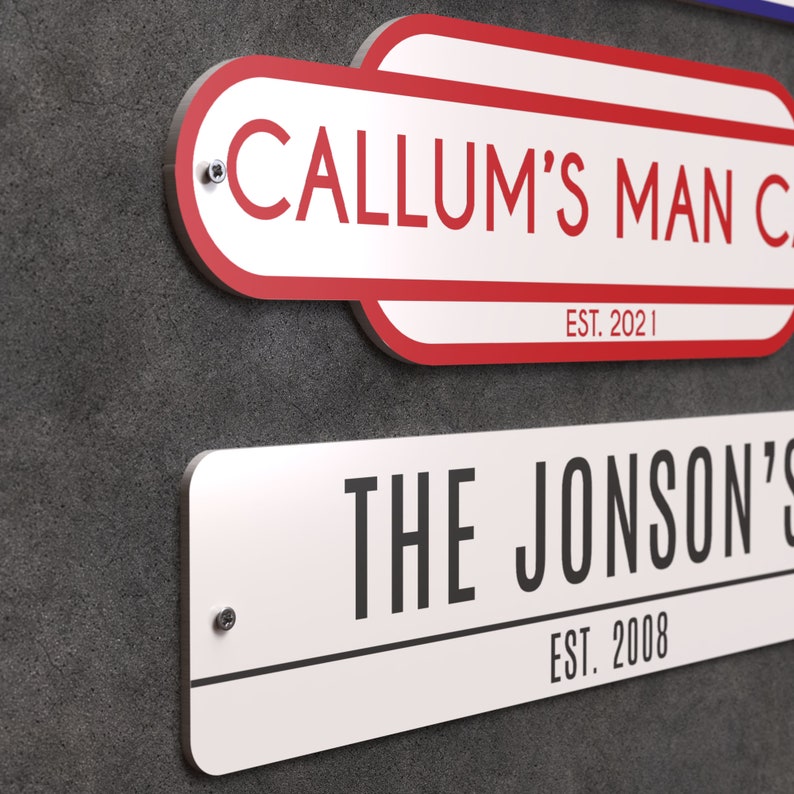 May include: Two personalised signs on a grey textured wall. The top sign, with red trim, reads "CALLUM'S MAN CAVE" and "EST. 2021". The bottom sign reads "THE JONSON'S" and "EST. 2008". Both signs are white with black text and mounted with screws.