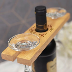 May include: Wooden wine bottle and glass holder with two glass holders and a bottle holder. The holder has a decorative floral design and the letter "A" engraved on it.