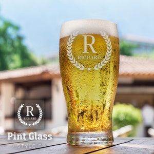 Op de afbeelding: Een helder pintglas met een gematteerde afwerking en een gepersonaliseerd ontwerp. Het glas heeft een krans met de letter "R" en de naam "Richard" gegraveerd in het glas. Het glas is gevuld met een goudgele vloeistof.
