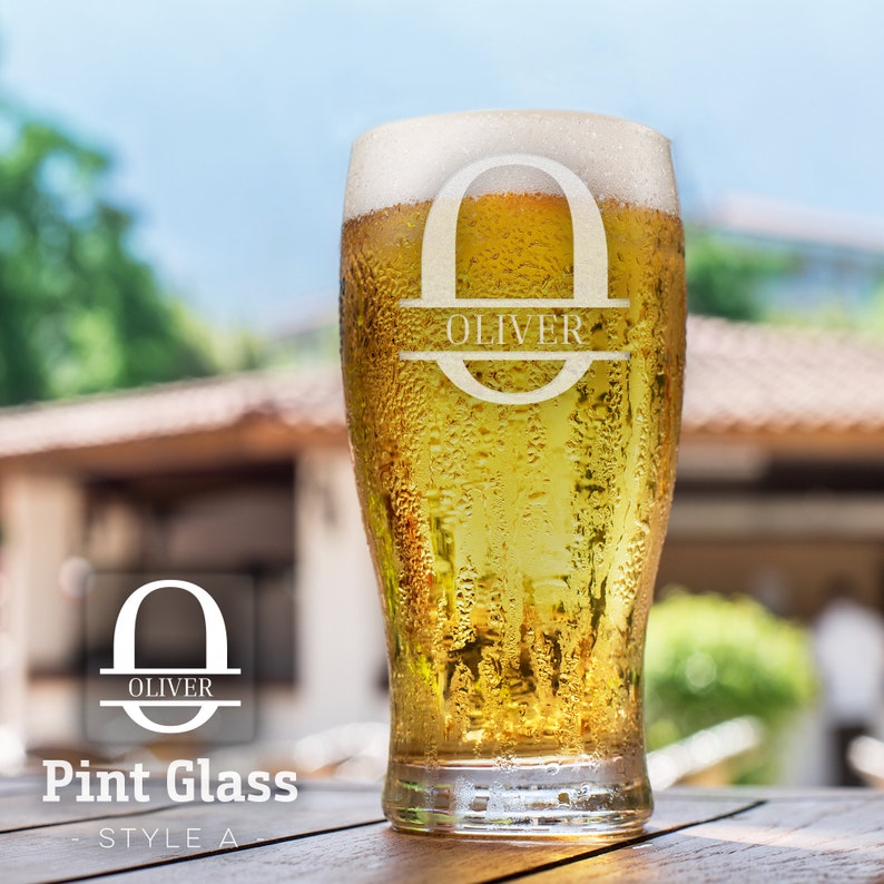 Op de afbeelding: Een gepersonaliseerd pintglas met de naam "Oliver" gegraveerd in een cirkelvormig ontwerp. Het glas is gevuld met een gouden drankje en heeft condensatie aan de buitenkant.