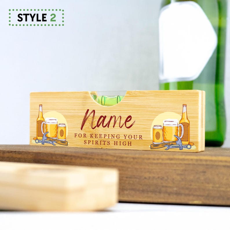 K&ouml;nnte beinhalten: Ein Holz-Wasserwaage mit einer gr&uuml;nen Libelle und einem bedruckten Design von Bierflaschen und Bechern. Die Wasserwaage tr&auml;gt den Text "Name for keeping your spirits high".