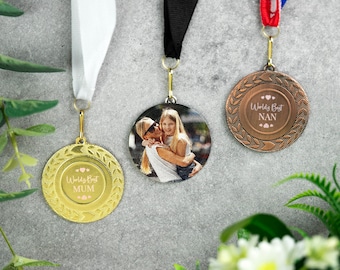 Peut inclure: Trois médailles dorées, bronze et argent avec des rubans. Les médailles présentent une photo de deux femmes qui s'embrassent et le texte "World's Best Mum" et "World's Best Nan".
