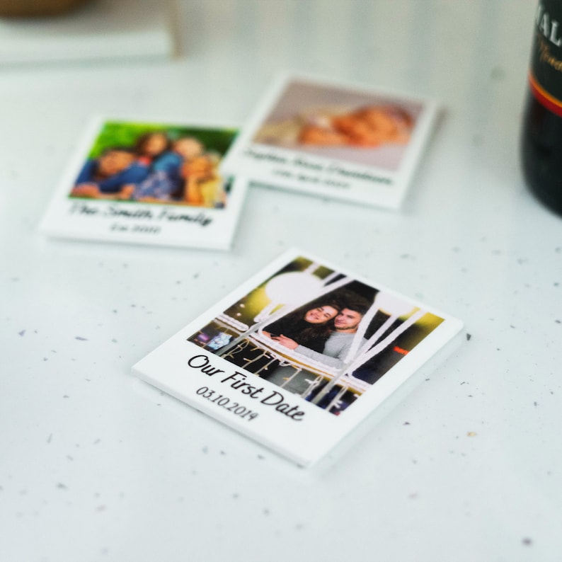 May include: A white square photo magnet with a picture of a couple on their first date. The magnet has the text "Our First Date" and the date "03.10.2014" printed on it.