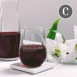 May include: A stemless wine glass with the text "YOUR NAME" etched on the side, filled with red wine. The glass is sitting on a white coaster.