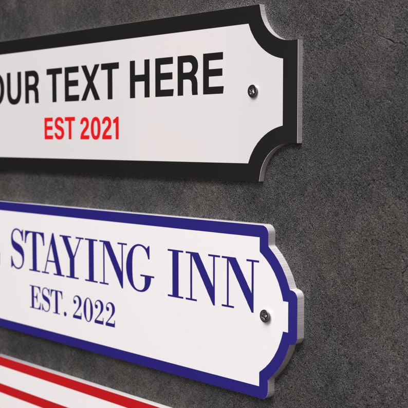 May include: White rectangular signs with decorative edges and text. One sign reads "YOUR TEXT HERE" and "EST 2021" in red. Another sign says "STAYING INN" and "EST. 2022" in blue. The signs are mounted on a grey wall.