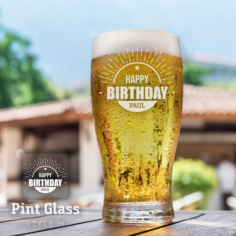 Op de afbeelding: Een bevroren pintglas met een gepersonaliseerd bericht dat "Happy Birthday Paul" luidt. Het glas is gevuld met een goudbruin bier en staat op een houten tafel.