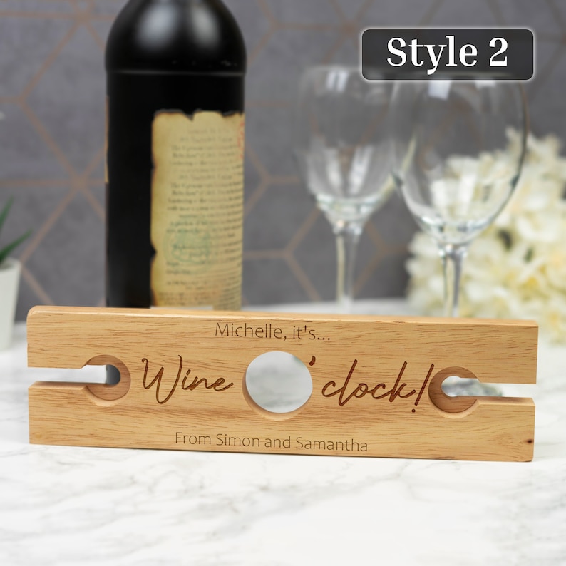 May include: Wooden wine bottle holder with two slots for glasses. It has the text "Michelle, it's... Wine 'o' clock! From Simon and Samantha" engraved on it.