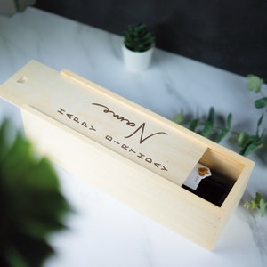 May include: A wooden box with a sliding lid, engraved with the text "Happy Birthday" and a name. The box is designed to hold a bottle of wine.
