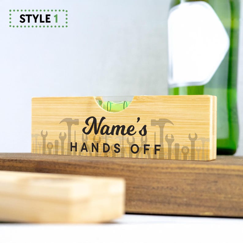 K&ouml;nnte beinhalten: Ein Holz-Wasserwaage mit einer gr&uuml;nen Blase und einer schwarzen Aufschrift "Name's Hands Off" mit einer Reihe von Werkzeugen, die auf die Oberfl&auml;che gedruckt sind.
