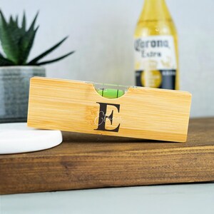 K&ouml;nnte beinhalten: Ein personalisiertes Bambus-Wasserwaage mit einer gr&uuml;nen Blase und dem Buchstaben "E" auf der Vorderseite graviert.