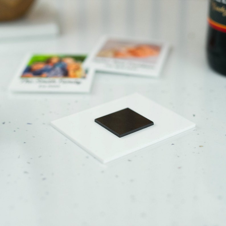 May include: A white square magnet with a black square magnet on top.