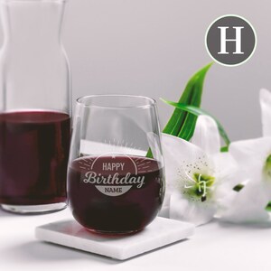 May include: A clear stemless wine glass filled with red wine. The glass has an etched design that says "Happy Birthday NAME".
