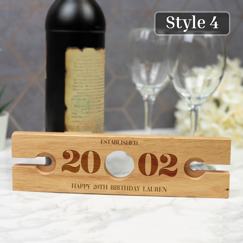 May include: Wooden wine bottle holder with two slots for glasses. It is engraved with "Established 2002" and "Happy 20th Birthday Lauren".