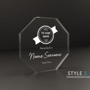 May include: A clear octagonal acrylic award plaque with a white star-shaped seal that reads "The Name Award". The plaque has the text "Awarded to Name Surname" and "Year/Date" below the seal.