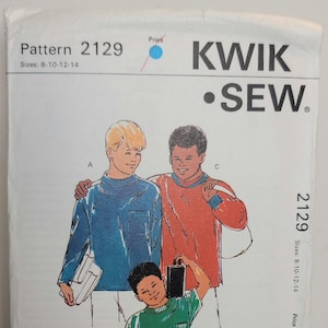 May include: Kwik Sew pattern 2129 for sizes 8-10-12-14. The envelope features illustrations of three individuals wearing long-sleeve and short-sleeve shirts. Text includes the brand name, pattern number, size range, and contact information for a sewing centre.