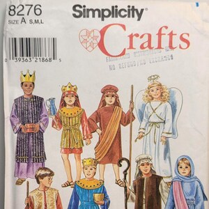 Op de afbeelding: Een Simplicity Crafts naaipatroon envelop, nummer 8276, maat A S,M,L. De illustratie toont zeven figuren in kerststal-kostuums, waaronder koningen, herders en een engel, gekleed in gewaden, tunieken, kronen en met staven in de hand.
