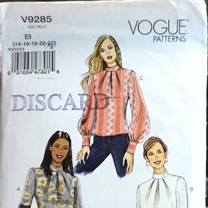 May include: A Vogue Patterns sewing pattern envelope V9285 for sizes 14-18-20-22. The cover features illustrations of three high-neck blouses with long sleeves, including one with a floral print and bell sleeves, and one with a geometric pattern.