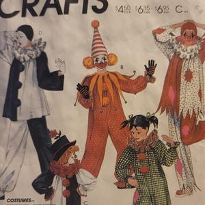 Op de afbeelding: Een vintage McCall's Crafts patroon envelop met illustraties van clown kostuums. De ontwerpen omvatten verschillende clown outfits met verschillende kleuren en patronen, waaronder stippen, ruiten en strepen. De tekst op de envelop bevat het woord "COSTUMES".