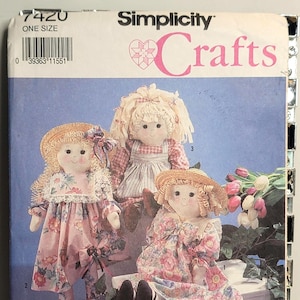 May include: A Simplicity Crafts pattern envelope, number 7420, featuring illustrations of three handmade fabric dolls. The dolls have yarn hair, straw hats, and floral dresses. The text includes '7420', 'ONE SIZE', 'Simplicity', 'Crafts', and 'PATTERN/PATRON'.