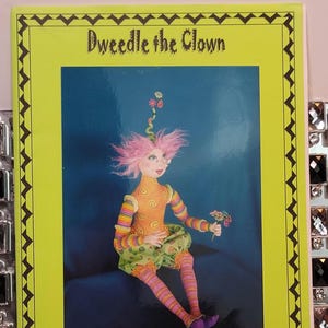 May include: A rectangular pattern envelope titled Dweedle the Clown with a lime green border and a black zigzag frame. The center image shows a doll with pink hair, an orange spiral-patterned top, green polka-dot pants, and striped leggings.
