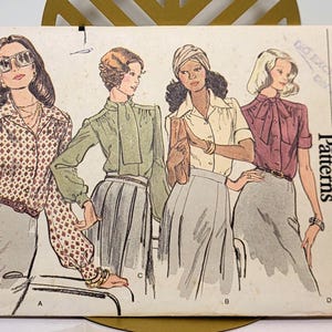以下が含まれることがあります： Very Easy Vogue Patternsの裁縫型紙封筒、番号8749、サイズ8。表面にはブラウスとスカートの4つの衣装のイラストが描かれています。テキストには「Very Easy Vogue Patterns」、「size 8」、「8749」、「suitable for knits」が含まれています。