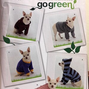 May include: A Simplicity sewing pattern envelope 2755 for dog clothing in sizes XS, S, and M. The front features four photographs of small dogs wearing various sweaters and hoodies, with the text go green and raise awareness four paws at a time.