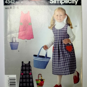 May include: A Simplicity sewing pattern envelope, number 4342, for a sleeveless pinafore dress and a tote bag. The cover features illustrations and a photograph of the finished garments, including a plaid dress with heart-shaped pockets and a blue tote.
