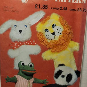 May include: A Style craft pattern envelope featuring illustrations of four hand puppets: a white rabbit with a red polka dot bow tie, a yellow lion with a yarn mane, a green frog wearing a striped vest, and a black and white panda. The red cover includes text.