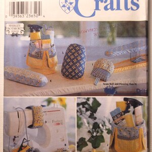 May include: A Simplicity Crafts sewing pattern envelope 9076 featuring instructions for fabric organizers, pressing hams, and sewing machine accessories. The cover displays blue and yellow floral patterned fabric items including a caddy, pin cushions, and a seam roll, with text labels and product codes.