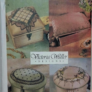 Può includere: Una busta per cartamodello Vogue Craft, numero 7251, con i design di Victoria Waller. La copertina mostra quattro scatole in tessuto decorative etichettate A, B, C e D, che presentano vari ricami, perline e decorazioni con nappe.