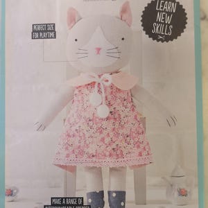 May include: A sewing kit for a dress-up kitty doll. The doll has a pink floral dress, blue denim-look shoes, and a white collar. The kit includes instructions to learn new skills and make interchangeable dresses. The text on the image says "Perfect size for playtime".