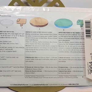 May include: A Simplicity 3664 sewing pattern envelope for a dog coat and pet bed. The back of the white paper envelope displays illustrations of the finished items in tan and blue, along with detailed instructions, fabric requirements, and a barcode.
