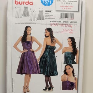Puede incluir: Un sobre de patrón de costura Burda 7571 para un vestido. El frente muestra ilustraciones y fotografías de dos variantes de vestido, una morada y otra verde oscuro, con tirantes finos, un corpiño ajustado y una falda acampanada.