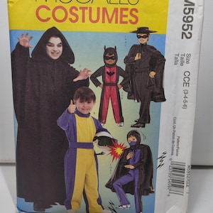 Może przedstawiać: Koperta z wykrojem krawieckim McCall's Costumes M5952 dla rozmiarów 3-4-5-6. Na froncie znajdują się ilustracje dzieci w różnych kostiumach, w tym czarna szata z kapturem, czerwono-czarny strój nietoperza, czarny kostium zamaskowanego bohatera, żółto-niebieski kombinezon oraz fioletowo-czarny strój ninja.