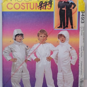 May include: A McCall's Costumes sewing pattern envelope, number 9493, featuring illustrations of children in white and silver hooded jumpsuits with American flag patches, and adults in black jumpsuits with blue accents on a purple and orange background.