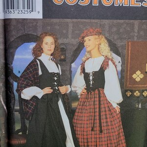Peut inclure: Patron de costumes Simplicity avec deux femmes vêtues de tenues médiévales. L'une porte une robe noire avec un sous-vêtement blanc et un châle à carreaux. L'autre porte une jupe à carreaux rouge, un corset noir et une blouse blanche.