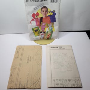 Butterick B4209 vintage hand puppet pattern envelope standing beside the uncut tissue and instruction booklet for the bear pig cat dog monkey mouse and bunny set