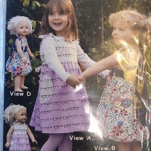 May include: A sewing pattern package showing two young girls in dresses, holding hands. The pattern includes matching doll dresses. The text on the package reads "Charley" and "Olive Ann Designs."