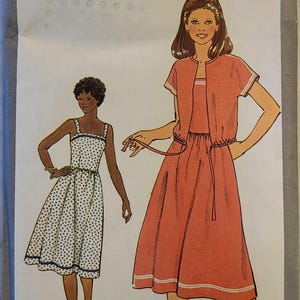 May include: Simplicity 8518 sewing pattern with illustrations of two dresses and a jacket. The pattern includes a polka dot dress and a coral-coloured dress with a matching jacket. The text "PATTERN/PATRON" and "MISS JEUNE FEMME" are visible.