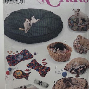 May include: A Simplicity Crafts sewing pattern envelope, number 9065, featuring illustrations of various pet accessories including round and rectangular pet beds, a woven basket, and bone-shaped mats with floral and plaid fabric designs.