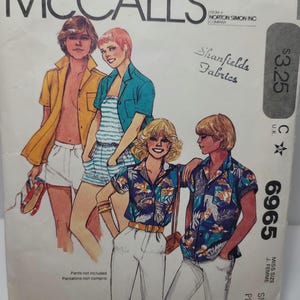 Op de afbeelding: Een vintage McCall's naaipatroon-envelop, nummer 6965, met illustraties van vier personen die verschillende overhemden, shorts en broeken dragen. De tekst bevat 'McCALL'S', 'Shanfields Fabrics', '6965', 'MISS SIZE' en 'SMALL PETITE'.