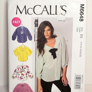 以下が含まれることがあります： サイズE5 (14-16-18-20-22)用McCall's M6648型紙封筒。表面には4種類のブラウスのバリエーションが掲載されています。ネイビーのドット柄トップス、黄色の半袖シャツ、蝶柄のブラウス、リボン付きの無地のピンクのトップスです。
