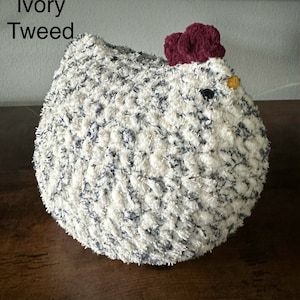 May include: A white and gray tweed chicken plush toy with a burgundy comb and a yellow beak. The toy is sitting on a wooden surface. Ivory Tweed.