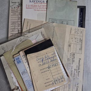 May include: A collection of vintage paper ephemera including a United States Savings Bond envelope, a Pennsylvania Power and Light Company bill, and a handwritten 1958 tax receipt. The documents feature various printed forms, grids, and text.