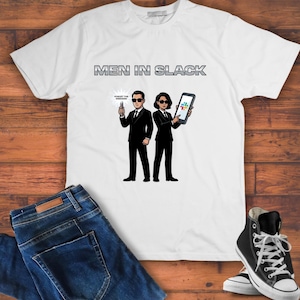 Puede incluir: Camiseta blanca con el texto "MEN IN SLACK" sobre una ilustración de dibujos animados de dos figuras con trajes negros y gafas de sol. Una figura sostiene un letrero que dice "FORGET THE WEEKEND", la otra una tableta.