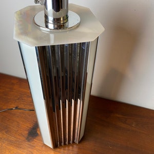Op de afbeelding: Een chromen en witte tafellamp met een geometrische basis en een geribbeld ontwerp. De lamp heeft een witte kap en een chromen steel.